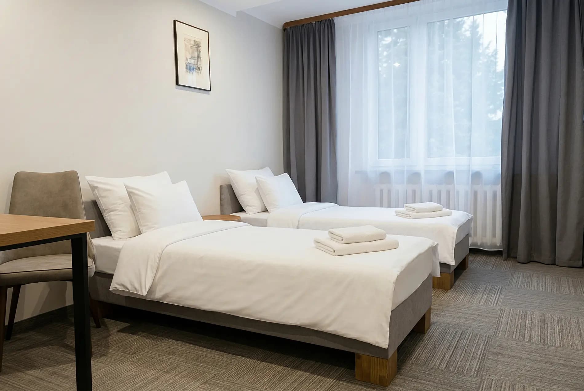 Komfortowy pokój dwuosobowy — jasne wnętrze z dwoma łóżkami, biurkiem i widokiem na park